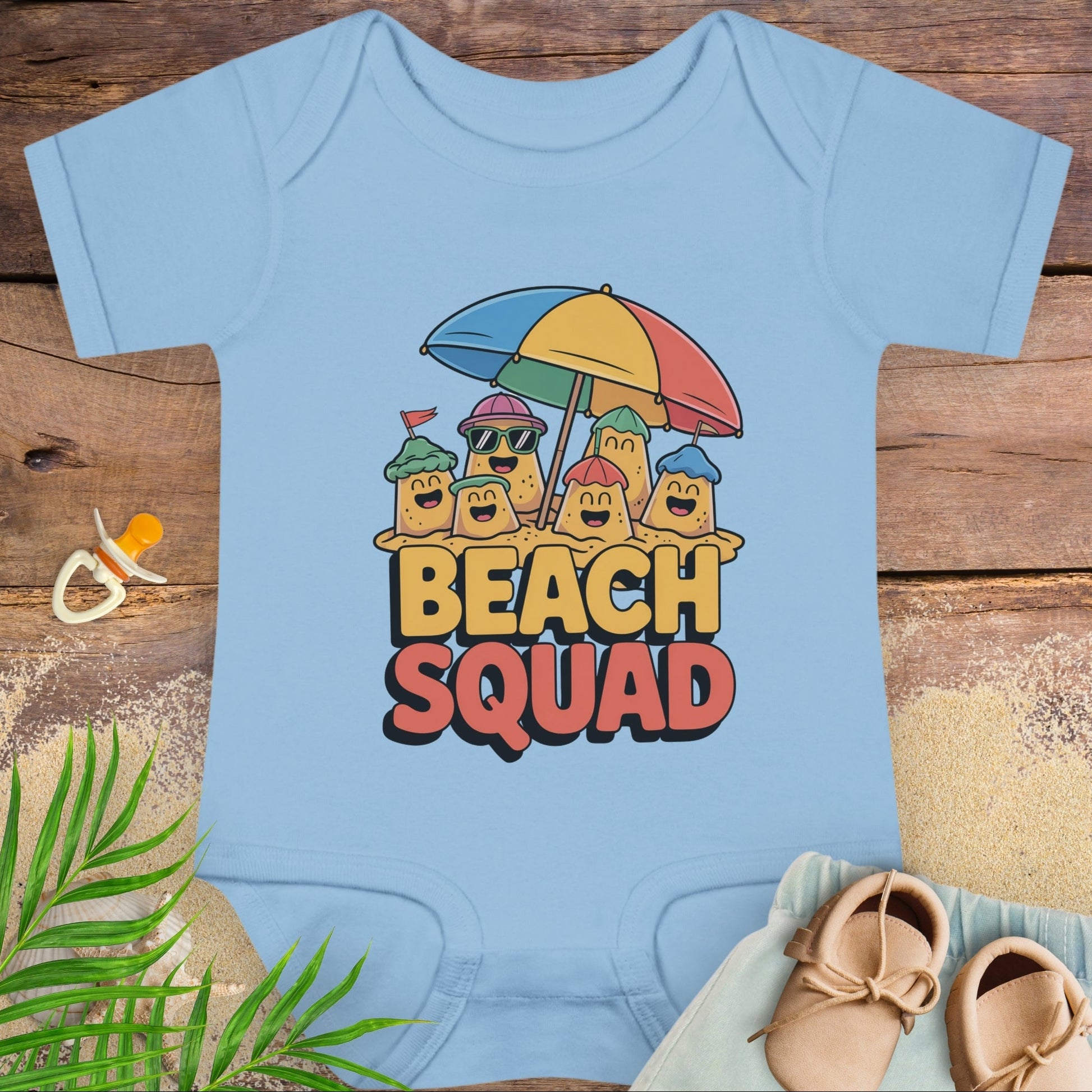 Baby onesie with 'Beach Squad' design on a wooden surface with beach accessories.