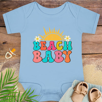 Baby onesie with 'Beach Baby' print on a wooden surface with beach-themed items.