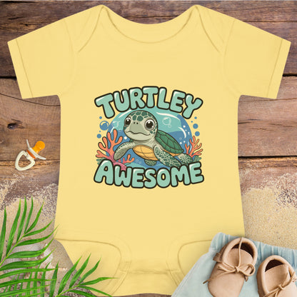 Yellow baby onesie with 'Turtley Awesome' graphic on a wooden surface with shoes and a pacifier.