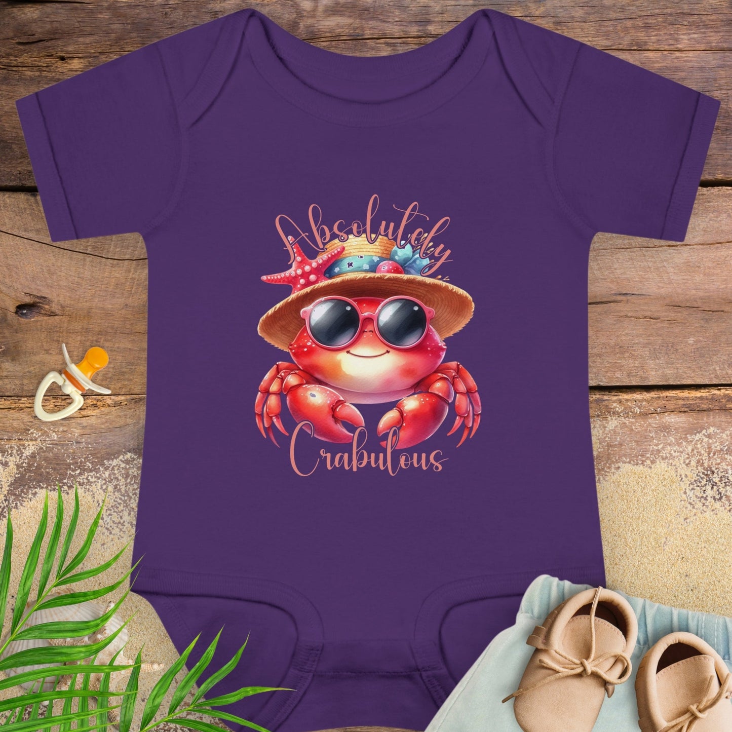 Purple baby onesie onesie with a crab design and 'Absolutely Crabulous' text on a wooden surface.