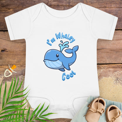 White baby onesie with blue whale design and text on a wooden surface with baby items.