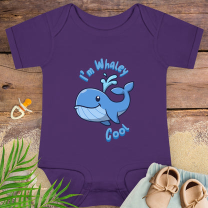 Purple baby onesie with a blue whale design and text on a wooden surface.