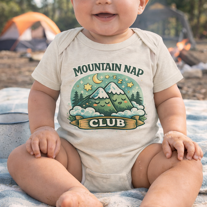 Baby wearing a onesie with 'Mountain Nap Club' design at a camping site.