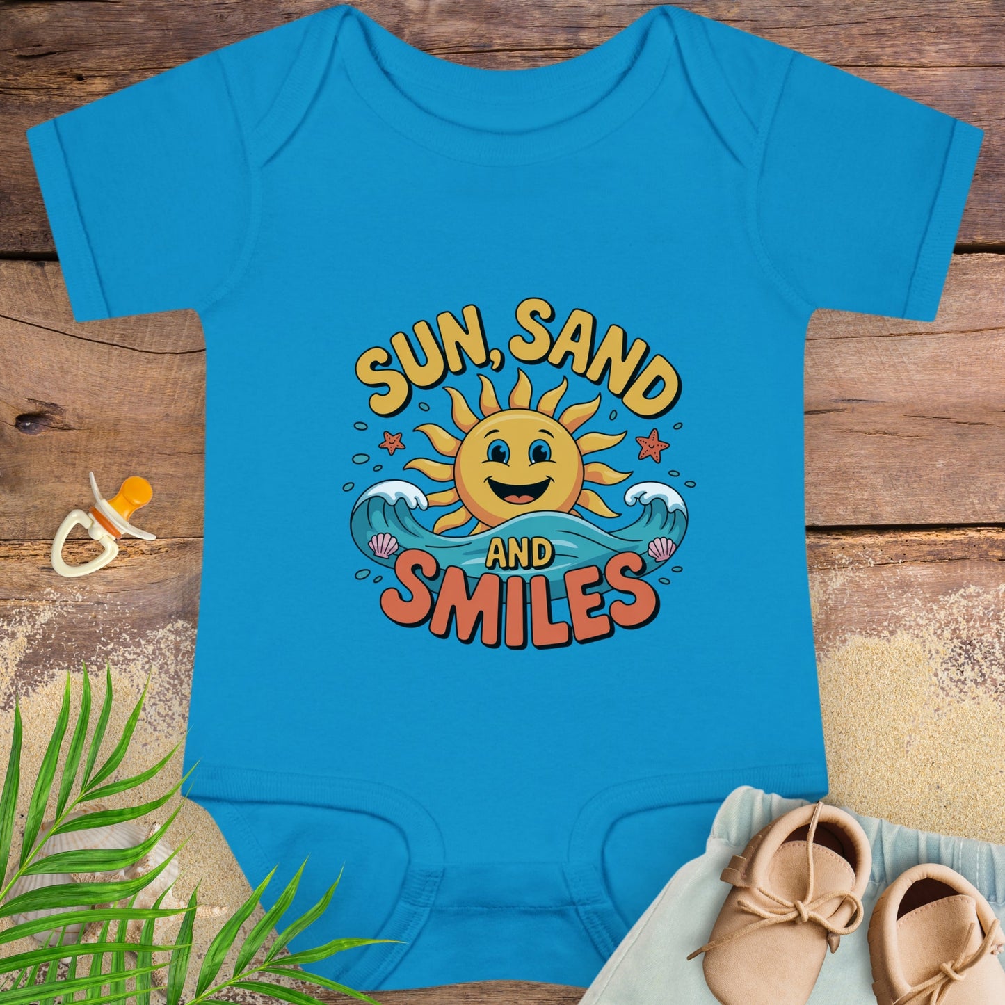Blue baby onesie with 'Sun, Sand and Smiles' design on a wooden surface with a pacifier and shoes.