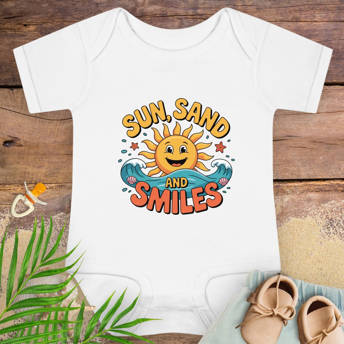 White baby onesie with 'Sun, Sand and Smiles' design on a wooden surface with beach-themed items.