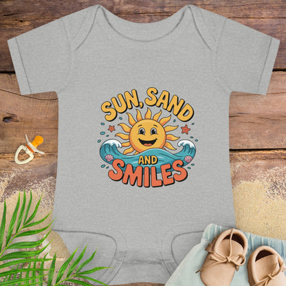 Gray baby onesie with 'Sun, Sand and Smiles' design on a wooden surface with baby items.