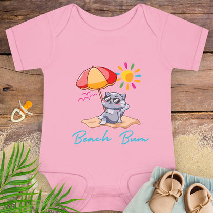 Pink baby onesie with a beach-themed design featuring a cat under an umbrella, sitting on sand under the sun.