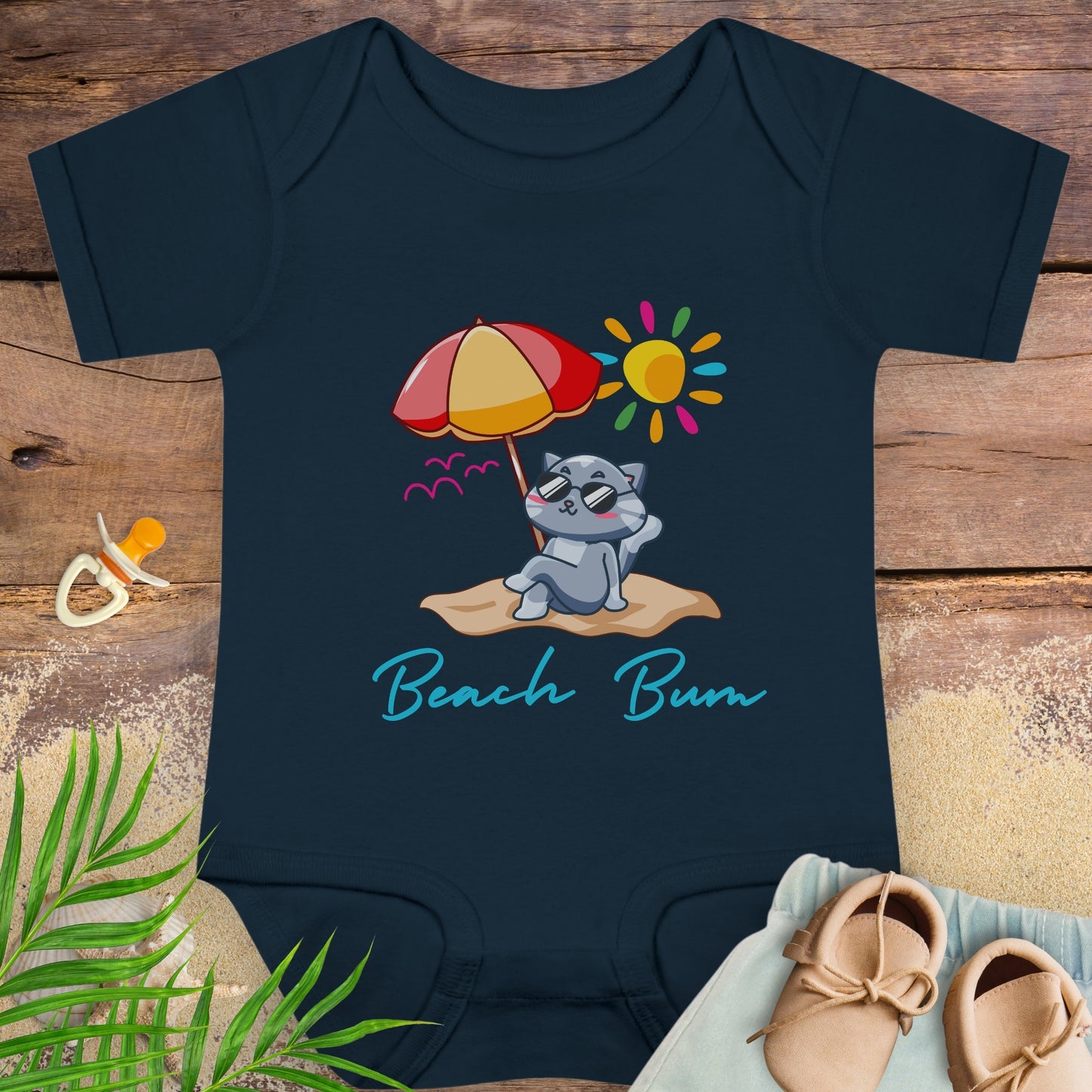 Navy blue baby onesie with a beach-themed design featuring a cat under an umbrella on a beach.