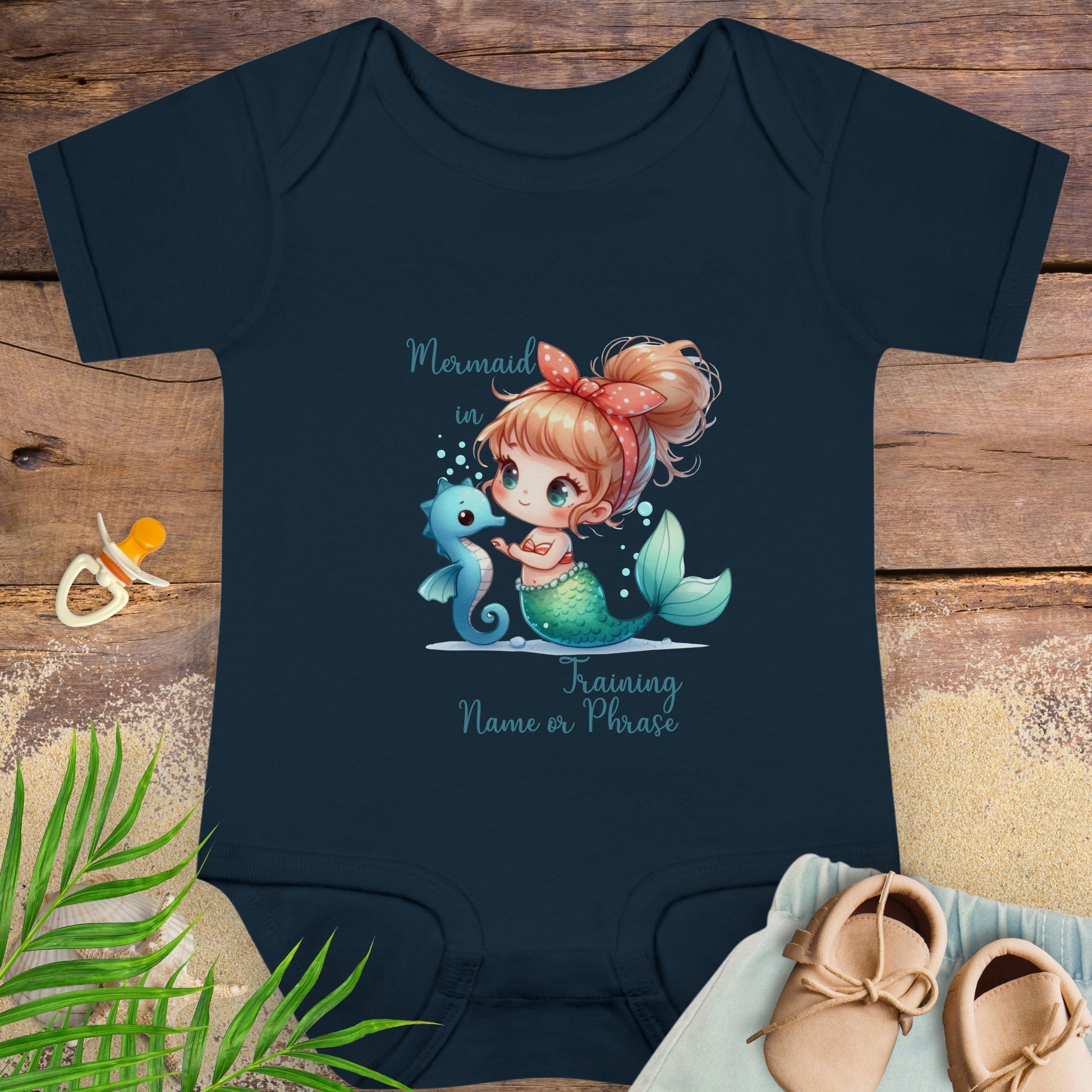 Navy blue baby onesie with mermaid design on a wooden surface with baby items.