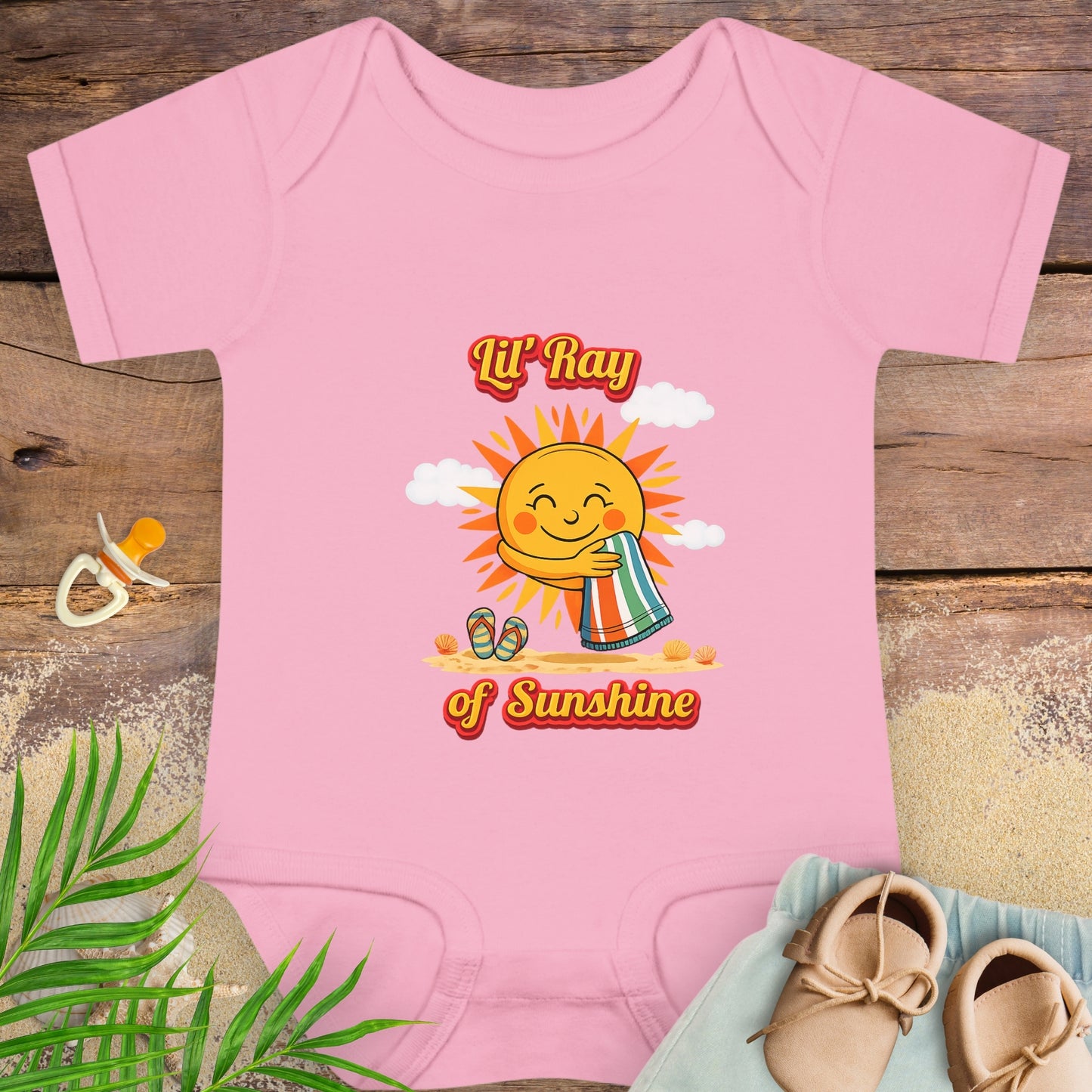 Pink baby onesie onesie with smiling sun beach graphic and text “Lil’ Ray of Sunshine.