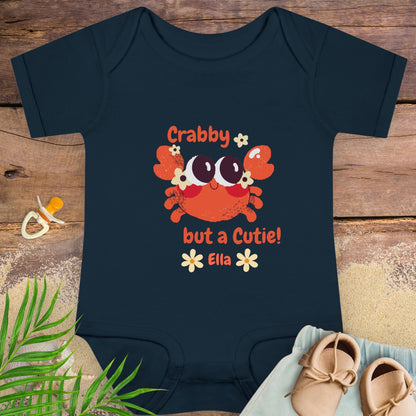 Navy blue baby onesie with a crab design and text on a wooden surface.