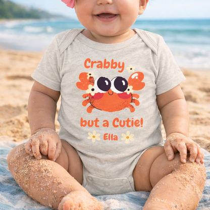 Baby wearing a crab-themed onesie on a beach