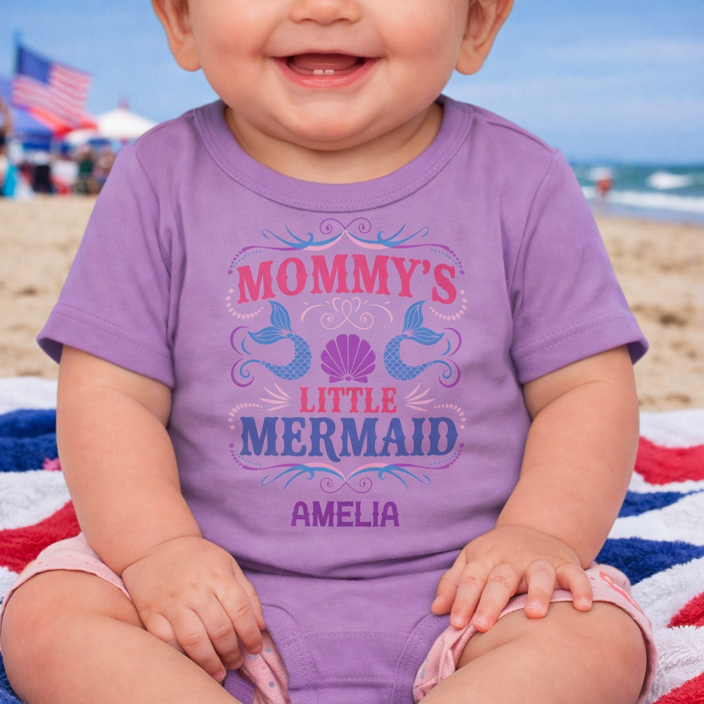 Child wearing a purple 'Mommy's Little Mermaid' shirt on a beach