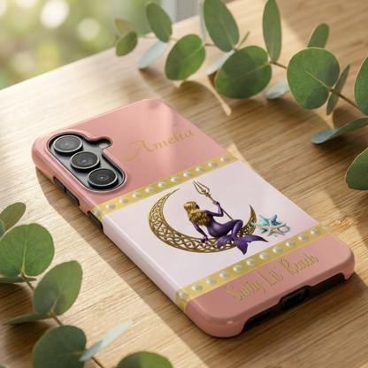 Phone case with a design of a mermaid and crescent moon on a pink background, placed on a wooden surface.
