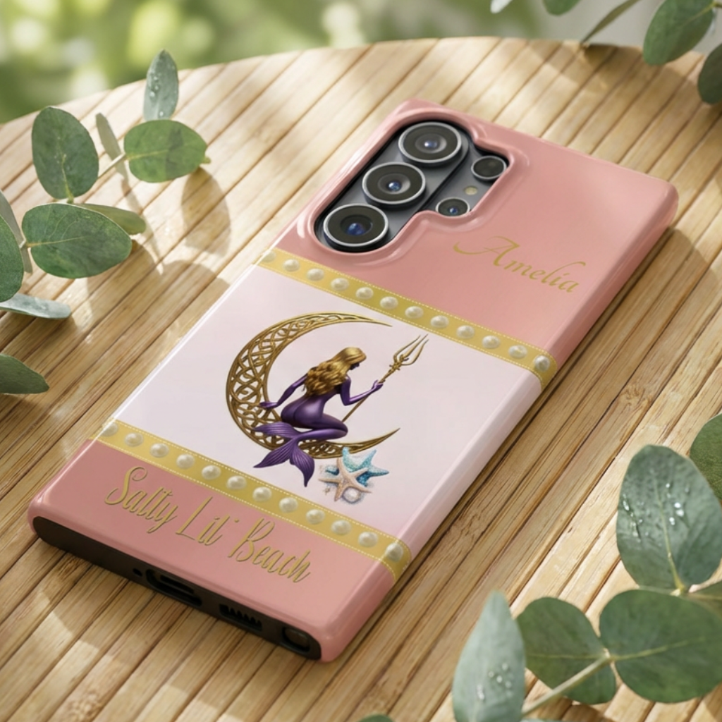 Phone case with a design of a mermaid and crescent moon on a pink background, placed on a wooden surface.