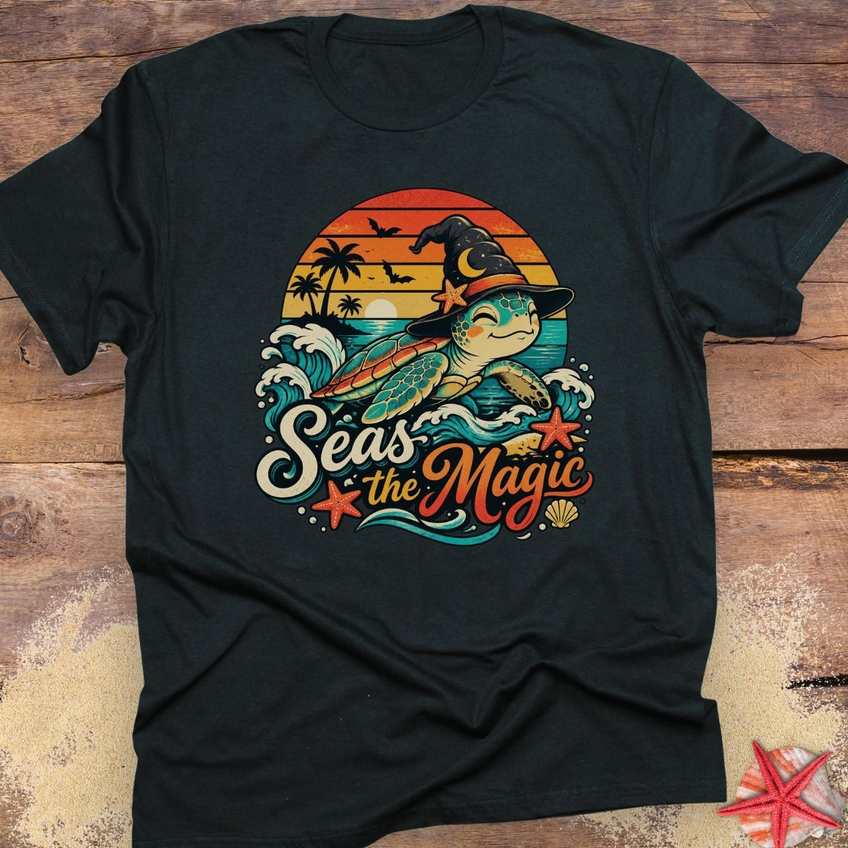 Black unisex t-shirt with “Seas the Magic” text, a sea turtle wearing a witch hat, ocean waves, sunset, palm trees, bats, and starfish.