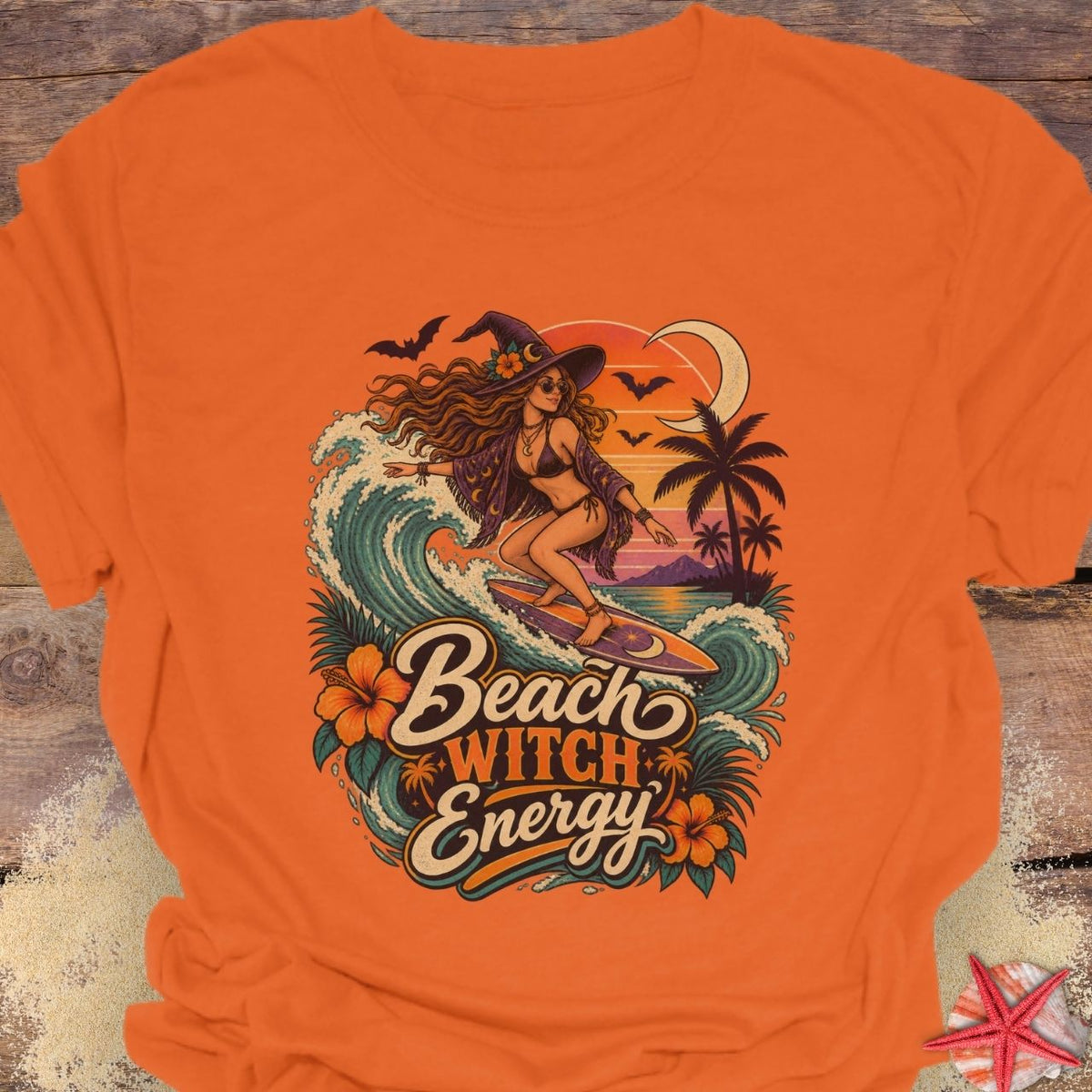 Orange unisex t-shirt with “Beach Witch Energy” text, a witchy surfer girl, ocean wave, sunset, crescent moon, bats, palm trees, and tropical flowers.