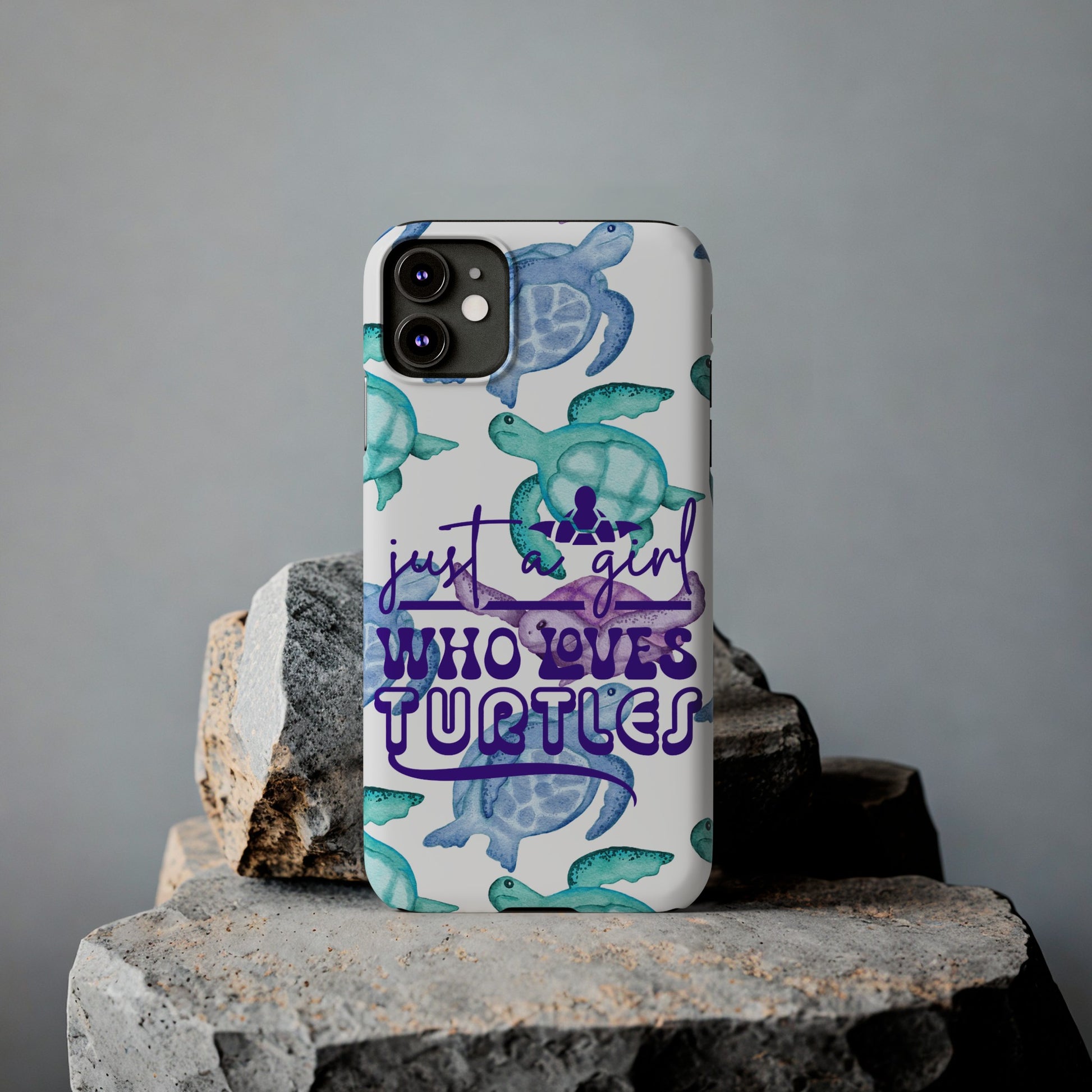 Iphone case with turquoise, blue and purple sea turtles that says  Just a Girl Who Loves Sea turtles laying against rock