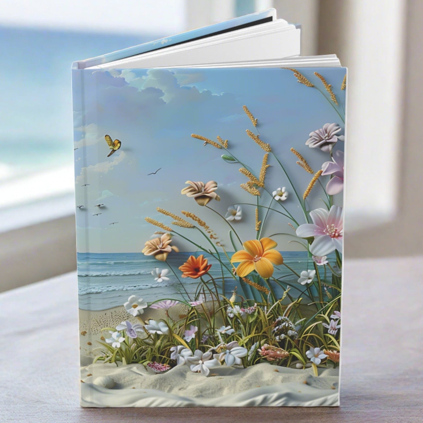 Hardcover journal with a scene of the beach with beach flowers and foliage standing on a table.