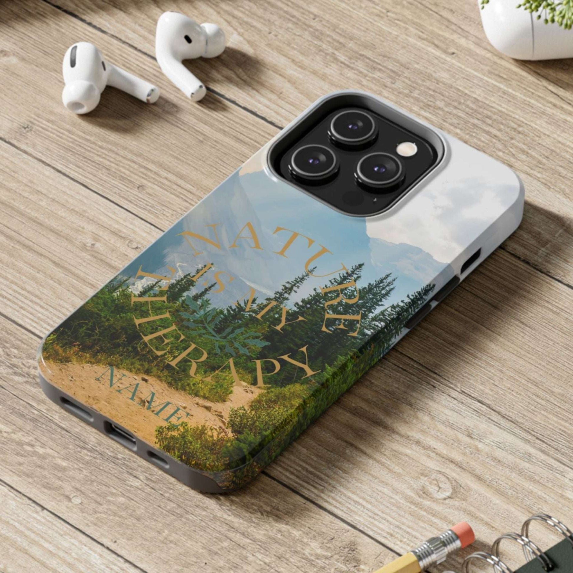 Phone case with nature design on a wooden desk with laptop, earbuds, and notebook.