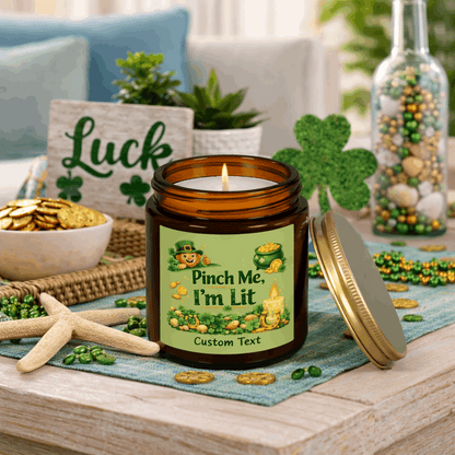 Amber candle jar with a lit candle, green label, and gold lid on with St. Patrick's Day Design and text Pinch Me, I'm Lit that can be personalized.