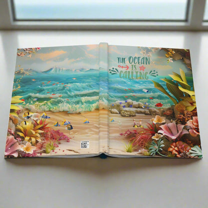 a hardcover journal laying open to show front and back with an ocean scene with flowers and the text the ocean is calling