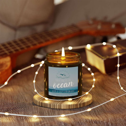 Candle in an amber jar with a label with an ocean scene and text 'Your vibe is the Ocean Keep it Calm and Bright'.