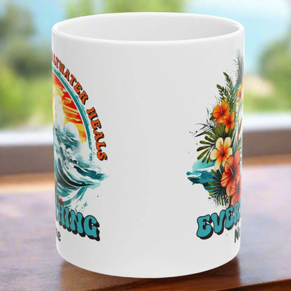 Side view of 10 oz. White ceramic mug with an ocean scene surrounded by tropical flowers with the text Saltwater Heals Everything and the word Name underneath where it can be personalized.