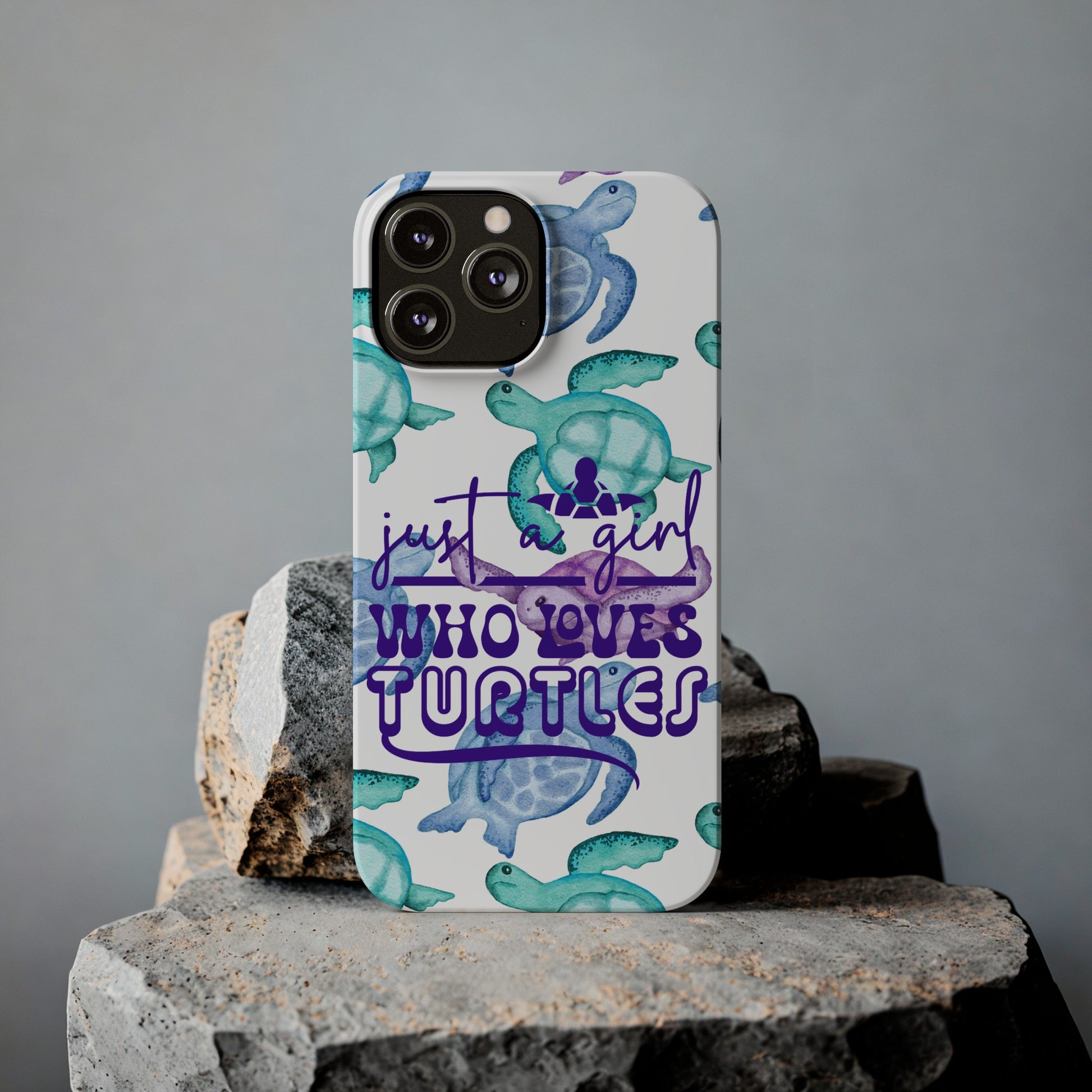 Iphone case with turquoise, blue and purple sea turtles that says  Just a Girl Who Loves Sea turtles laying against rock