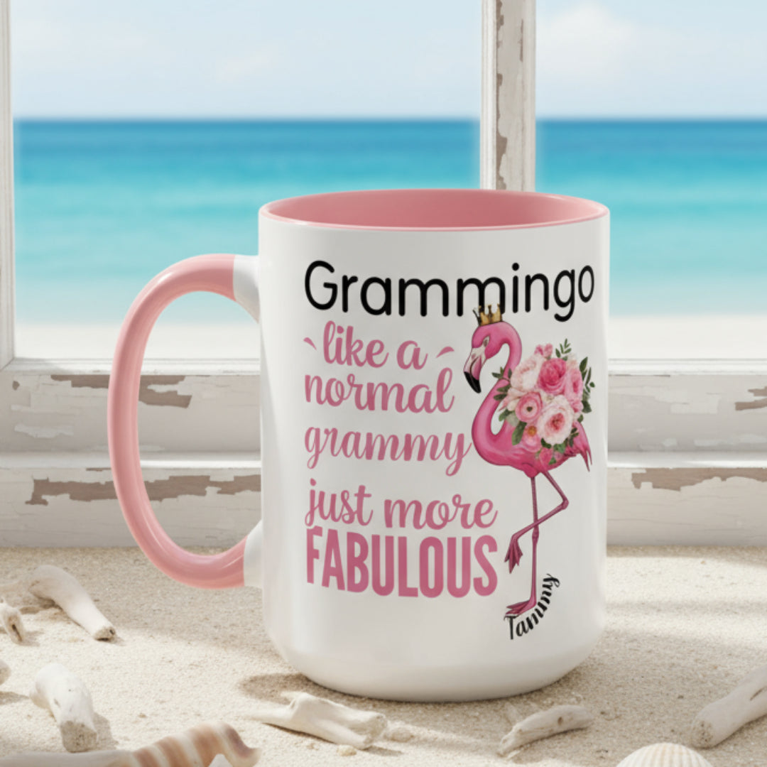 Ceramic coffee mug featuring a flamingo adorned with flowers and the text “Grammingo like a normal Grammy just more fabulous,” available with white, pink, or black handle options.
