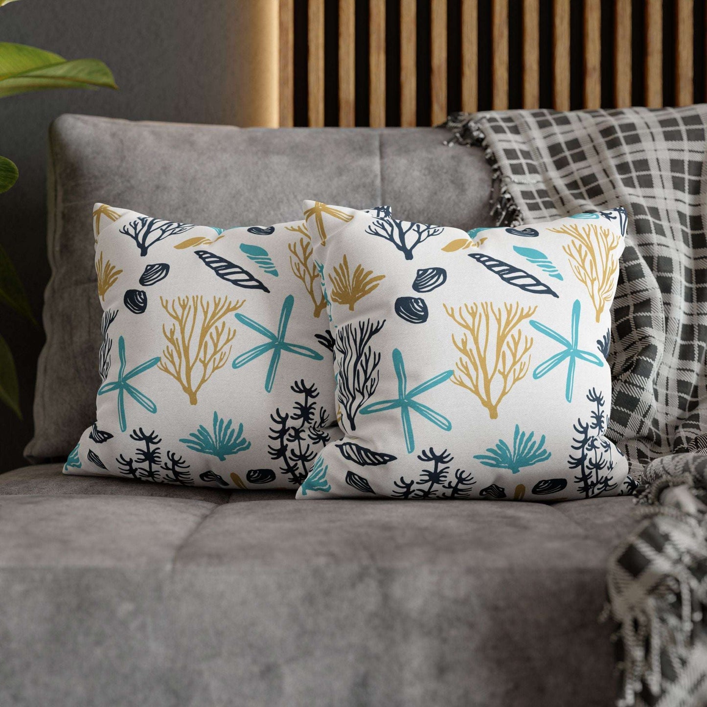 Two 14" x 14" white pillows with coral and starfish pattern on a gray couch.