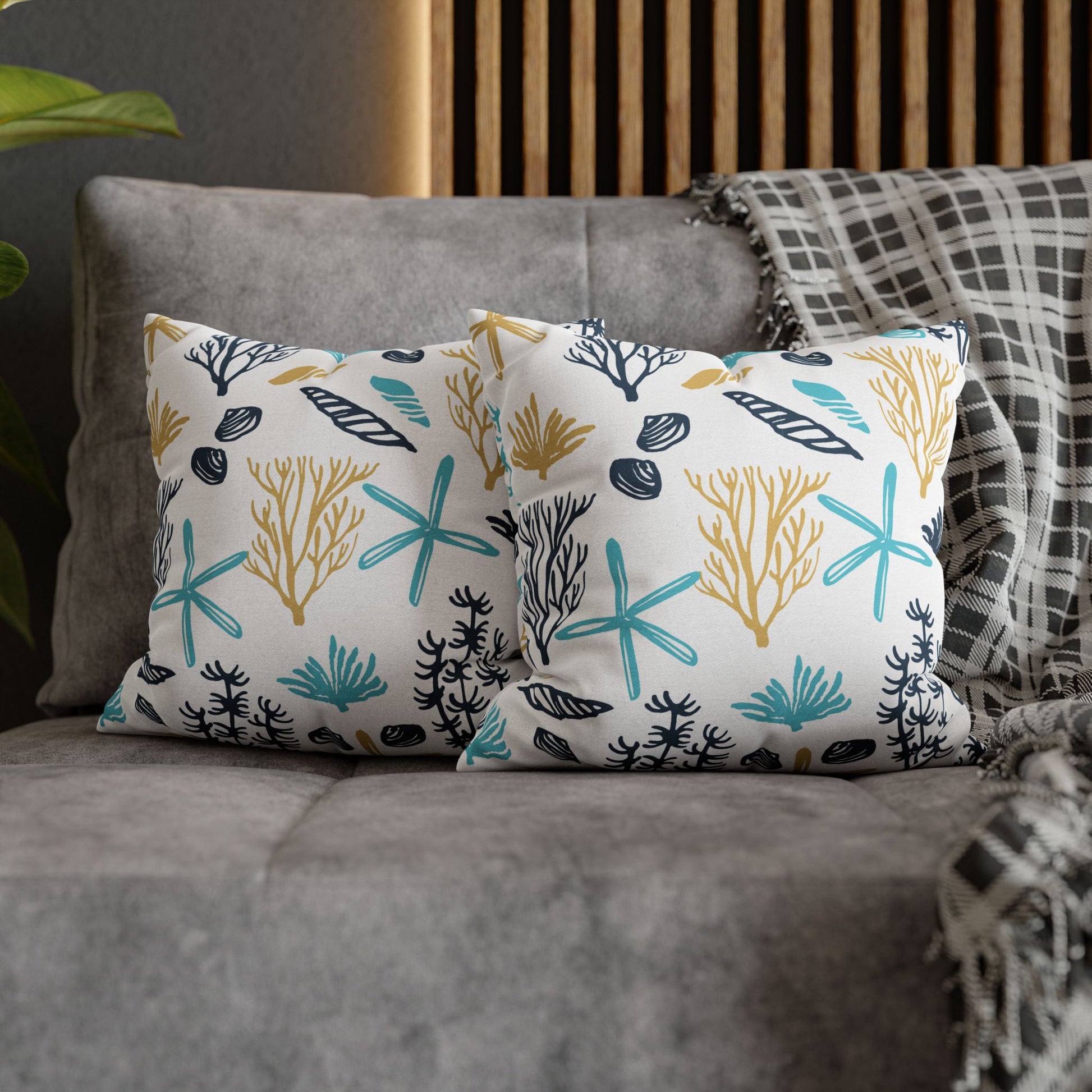 Two 14" x 14" white pillows with coral and starfish pattern on a gray couch.