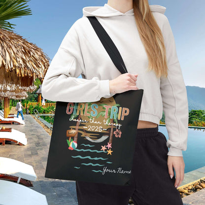 Person holding a 16" x 16" black tote bag with 'Girls Trip' beach design that can be personalized.