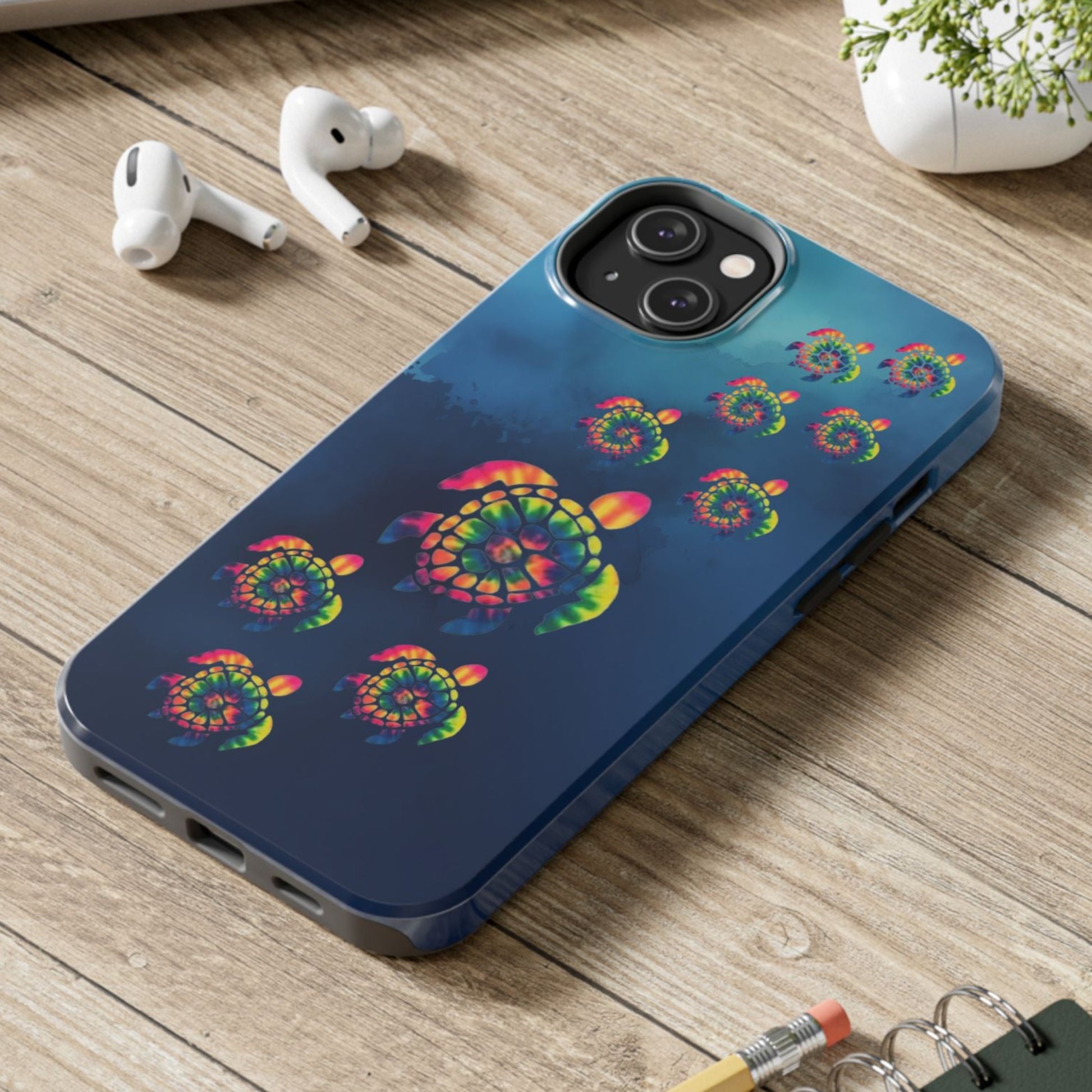 Phone case with colorful spiral design on a wooden surface with laptop, earbuds, and notebook.