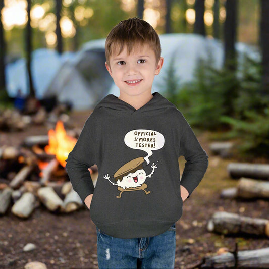 Boy wearing a vintage smoke cozy toddler hoodie with “Official S’mores Tester” speech bubble and a cartoon s'more  – cute outdoor-themed sweatshirt for little campers.