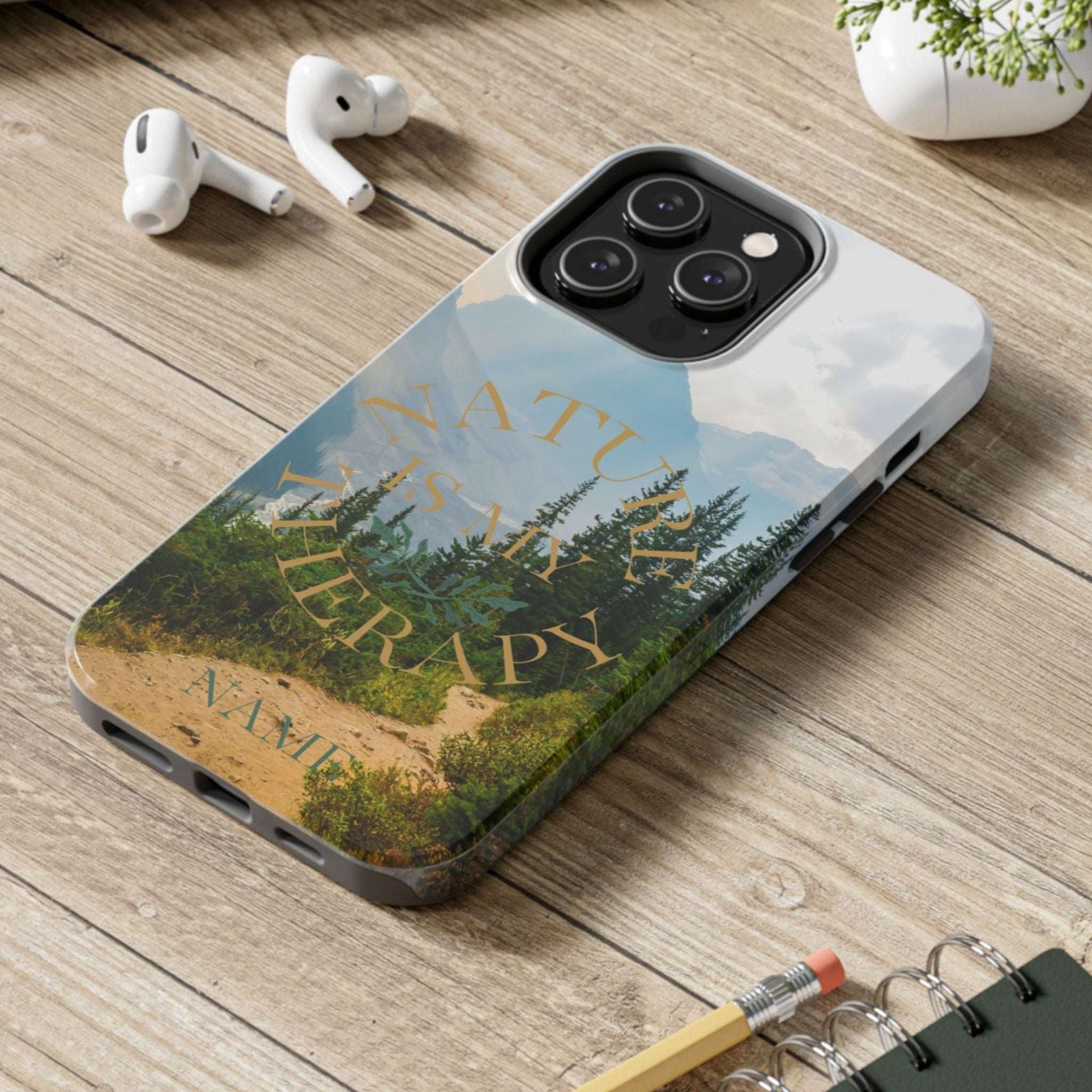 Phone case with nature design on a wooden surface with laptop, earbuds, and notebook.