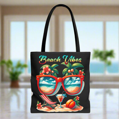 Black Tote bag featuring sunglasses with ocean and beach scene reflections, palm trees coming out of the glasses, a beach chair and cocktail on the sand, with the phrase "Beach Vibes" in a retro rainbow gradient font.