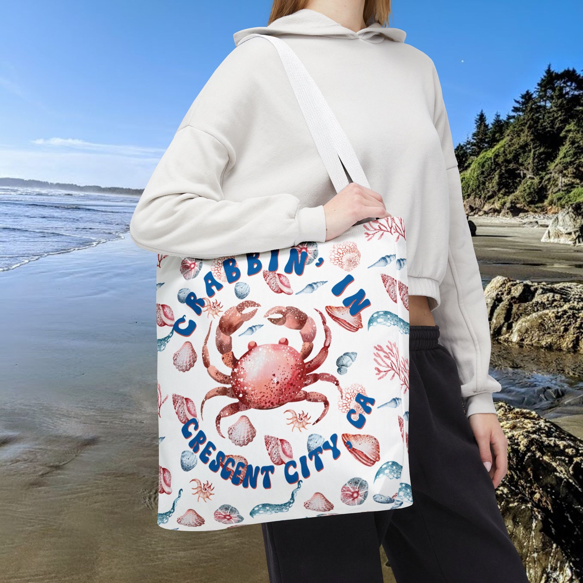 White 18" x 18" Tote bag featuring a crab surrounded by seashells and underwater life in blue and soft red tones with the phrase "Crabbin' in Crescent City, CA.