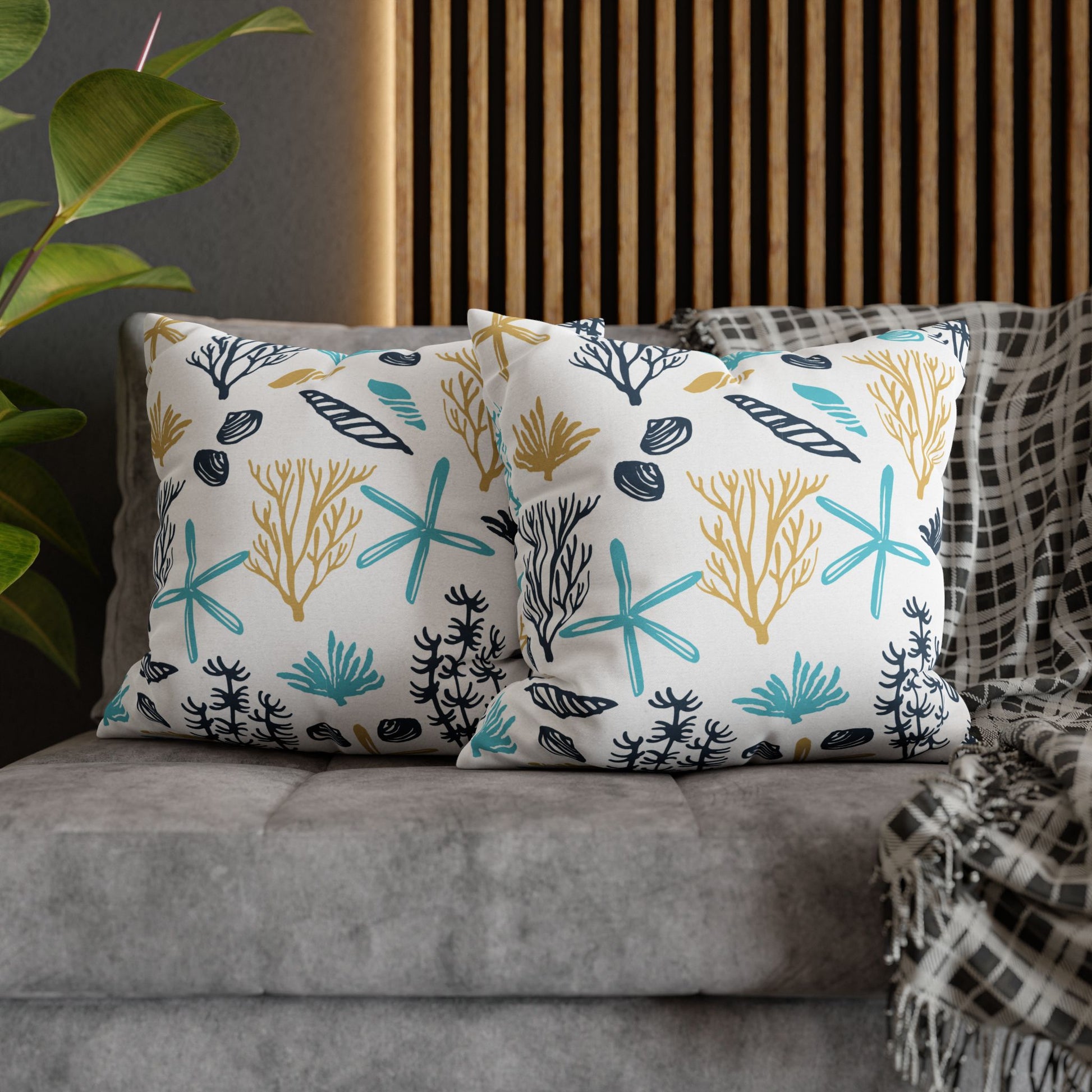 Two 20" x 20" white pillows with coral and starfish pattern on a gray couch.