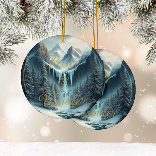 Round Christmas ornament with mountain and forest design, featuring 'Peace & Wonder' text, hanging against a snowy branch background.