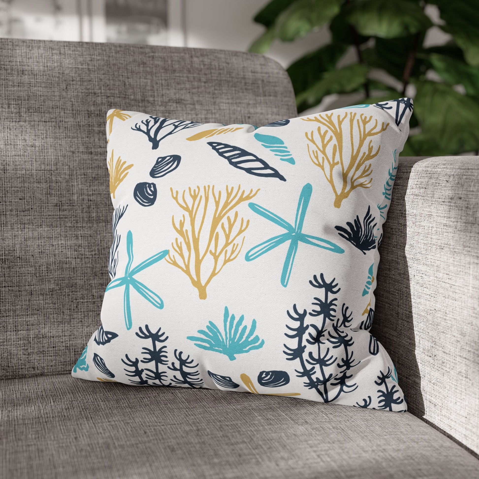 Decorative 16" x 16" white pillow with coral and starfish pattern on a gray couch.