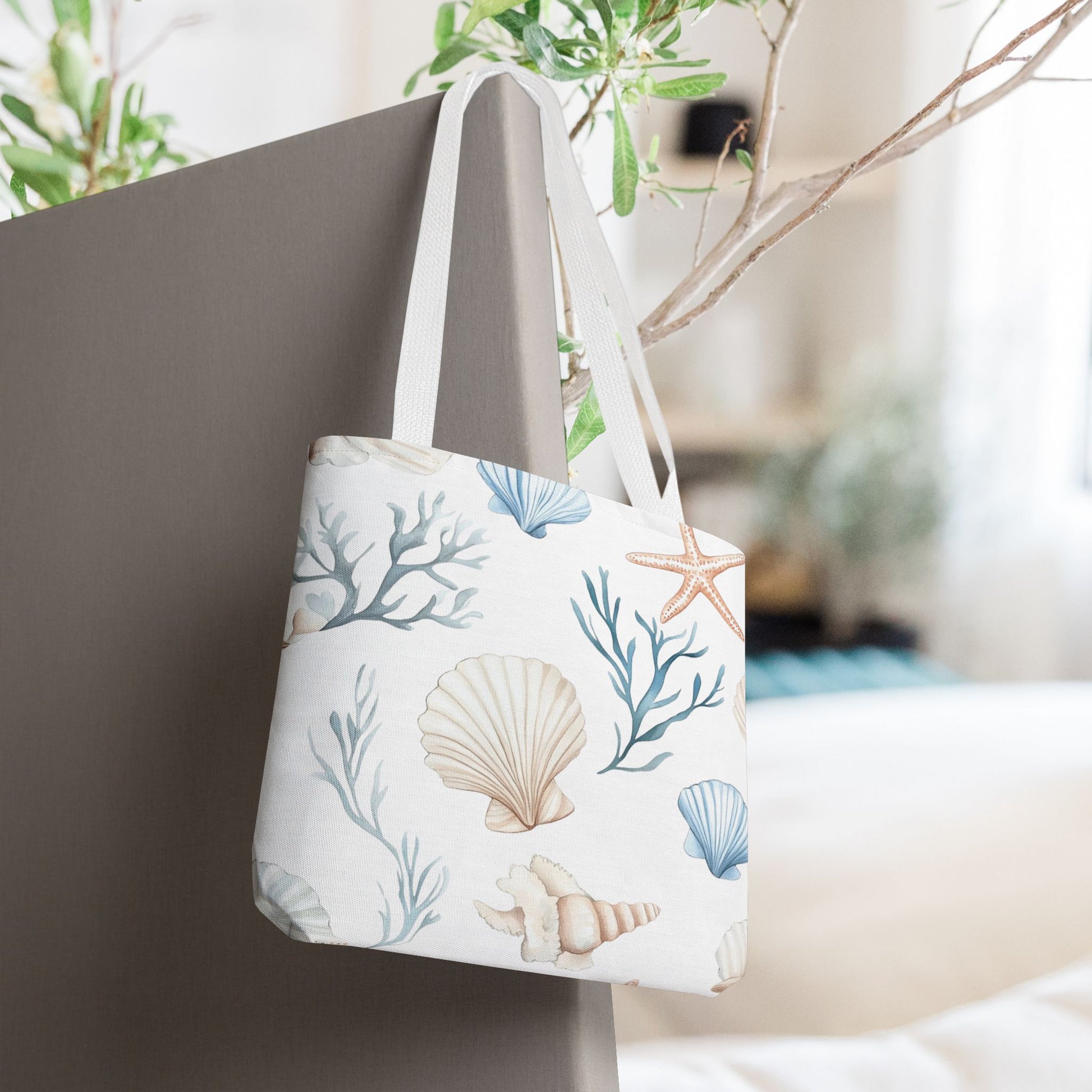 White tote bag with pastel blue and coral seashells, starfish, and underwater plants, with white handles.