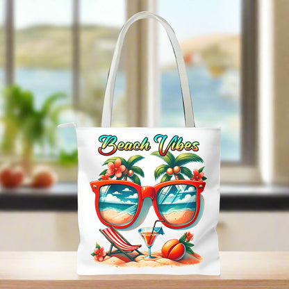 White Tote bag featuring sunglasses with ocean and beach scene reflections, palm trees coming out of the glasses, a beach chair and cocktail on the sand, with the phrase "Beach Vibes" in a retro rainbow gradient font.