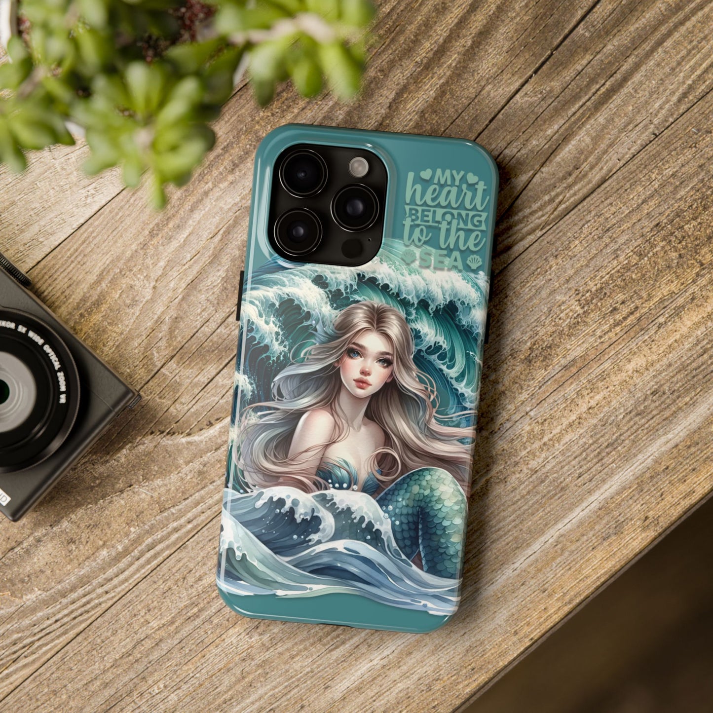 Phone Case with Flowy mermaid with ocean wave behind and text My Heart Belongs to the Sea laying on desk.