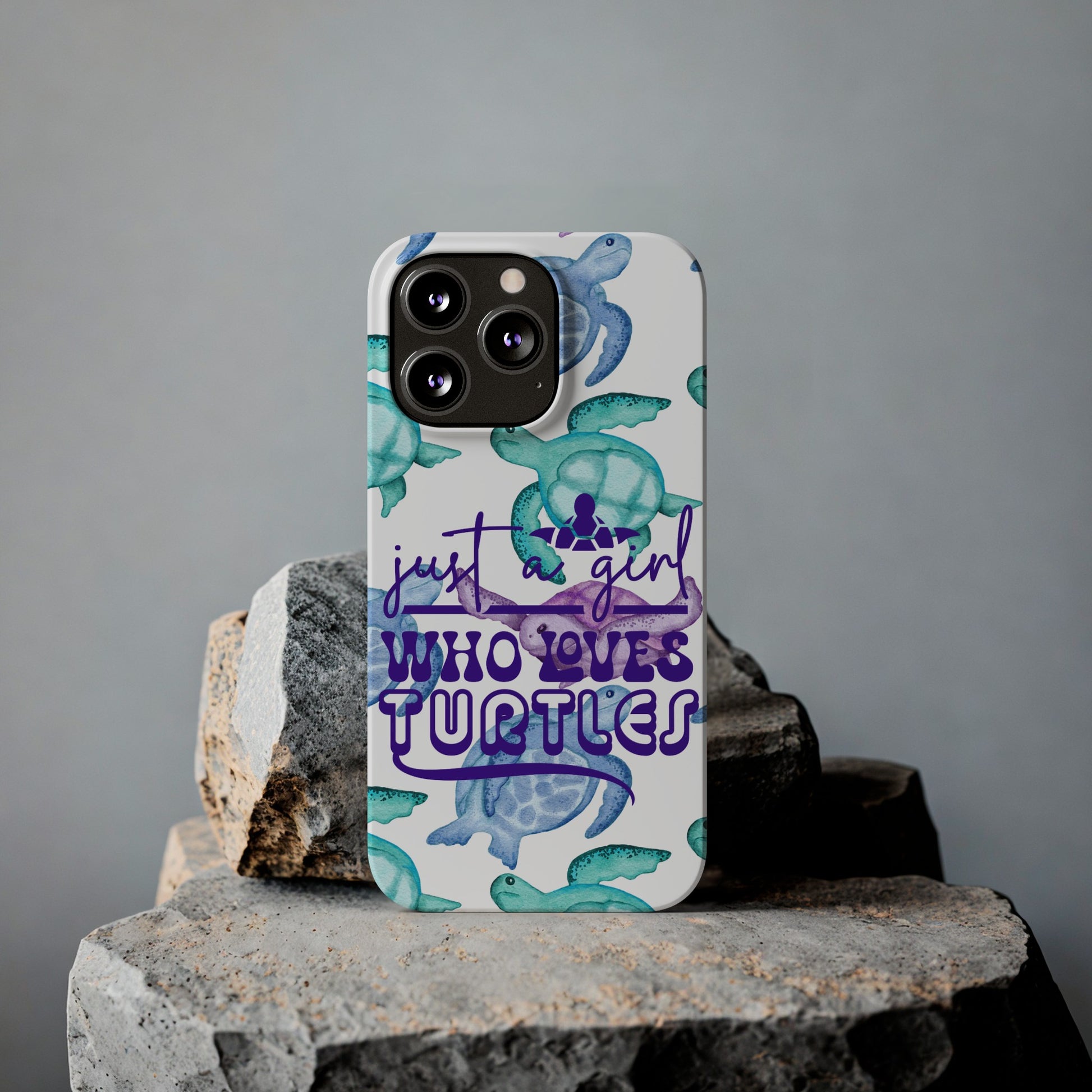 Iphone case with turquoise, blue and purple sea turtles that says  Just a Girl Who Loves Sea turtles laying against rock