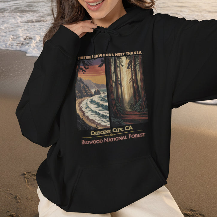 A woman wearing a black Crescent City California hoodie featuring vintage redwood forest and Pacific coast artwork with Where the Redwoods Meet the Sea design.