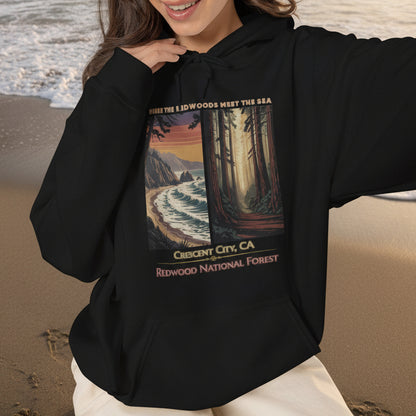 A woman wearing a black Crescent City California hoodie featuring vintage redwood forest and Pacific coast artwork with Where the Redwoods Meet the Sea design.