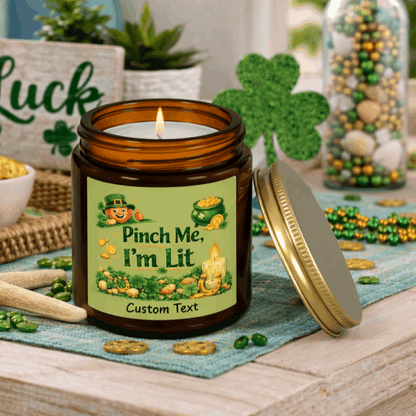 Amber candle jar with a lit candle, green label, and gold lid on with St. Patrick's Day Design and text Pinch Me, I'm Lit that can be personalized.