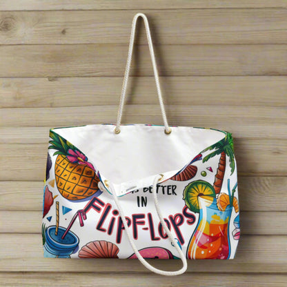 A weekender bag with a white background with pictures of a pineapple, cocktails, seashells and palm tree and says life is better in flip flops