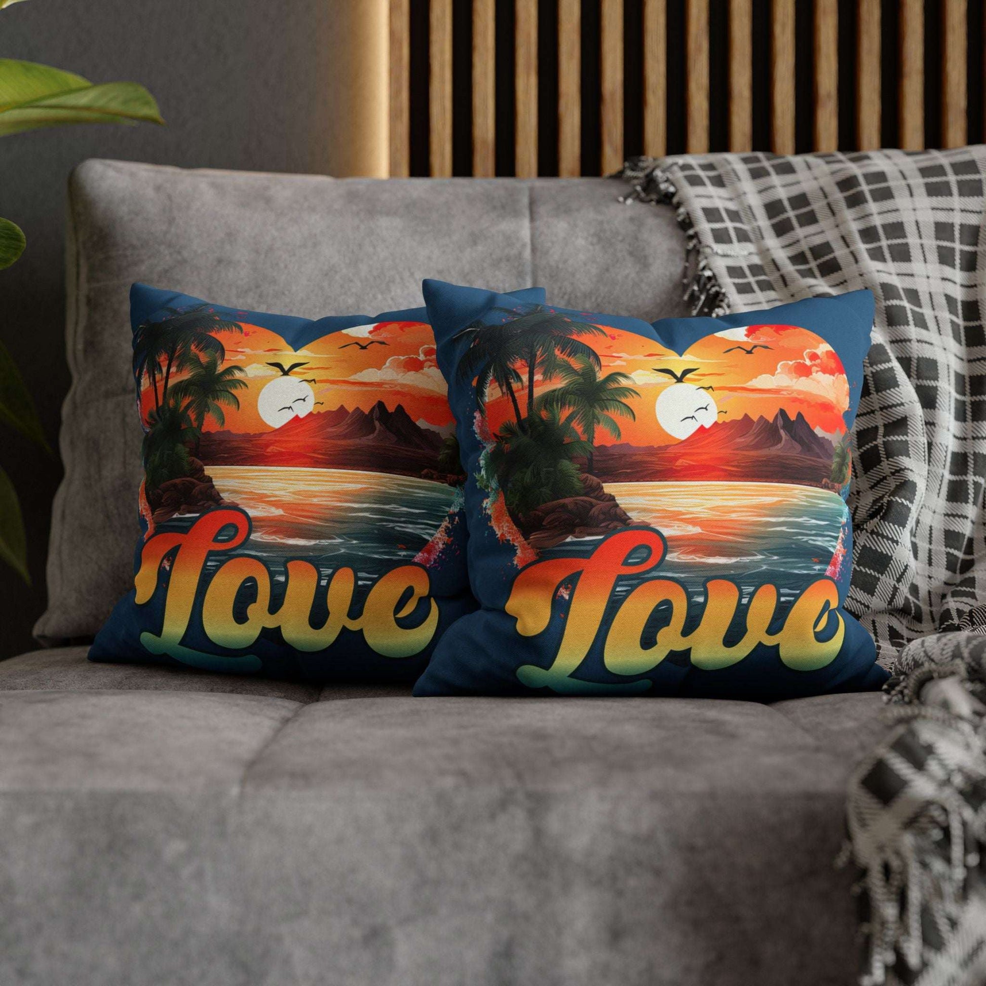 Two decorative 14" x 14" blue pillows with a sunset heart design and 'love' text on a gray couch.